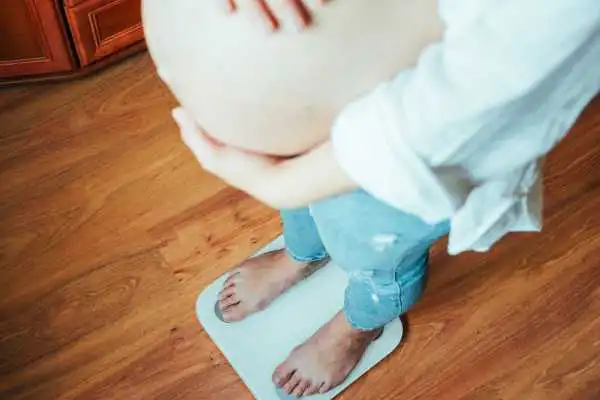 Image of woman weighing herself and experiencing weight gain through pregnancy Bolton